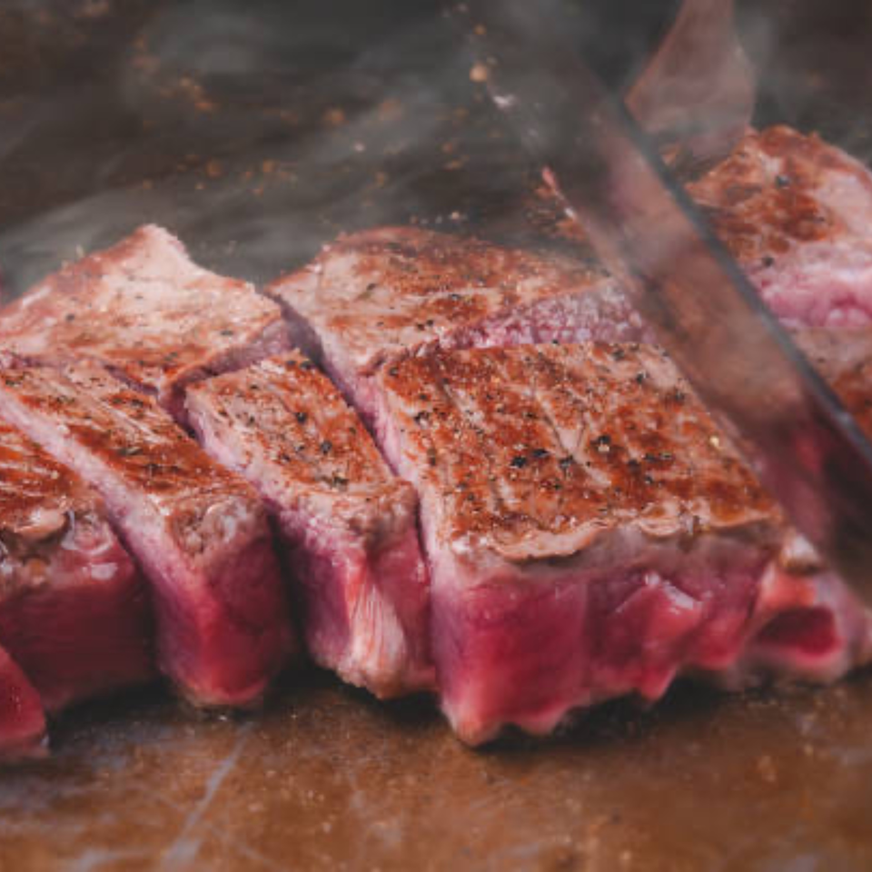 Sizzling, perfectly cooked steak, sliced into thick pieces with a knife, showing a pink center.