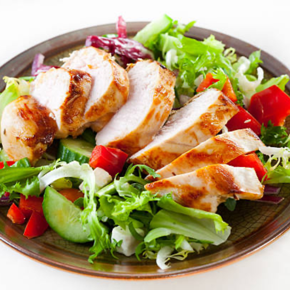 Grilled chicken breast slices on a bed of fresh green and red lettuce, cucumbers, and red bell peppers.