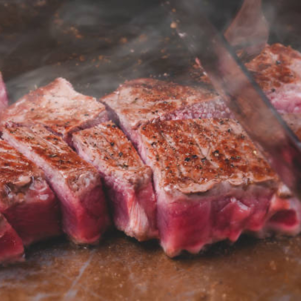 Sizzling, perfectly cooked steak, sliced into thick pieces, with a knife cutting another piece.