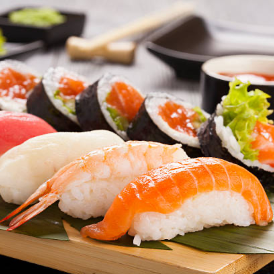 Assorted sushi and maki rolls, including salmon, tuna, and shrimp, on a wooden board.