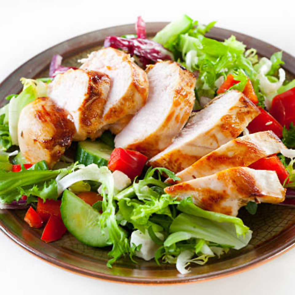 Grilled chicken breast slices on a fresh green salad with red bell peppers and cucumbers.