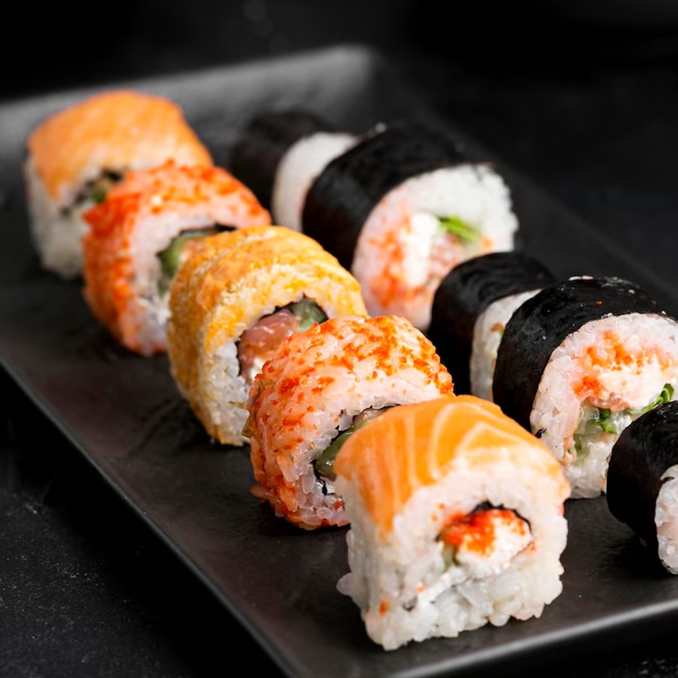 A black platter displays various sushi rolls, including salmon, tobiko, and nori-wrapped options.