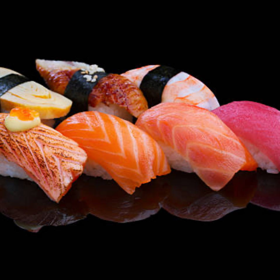 A close-up of various nigiri sushi pieces, including salmon, tuna, shrimp, and eel, on a dark surface.