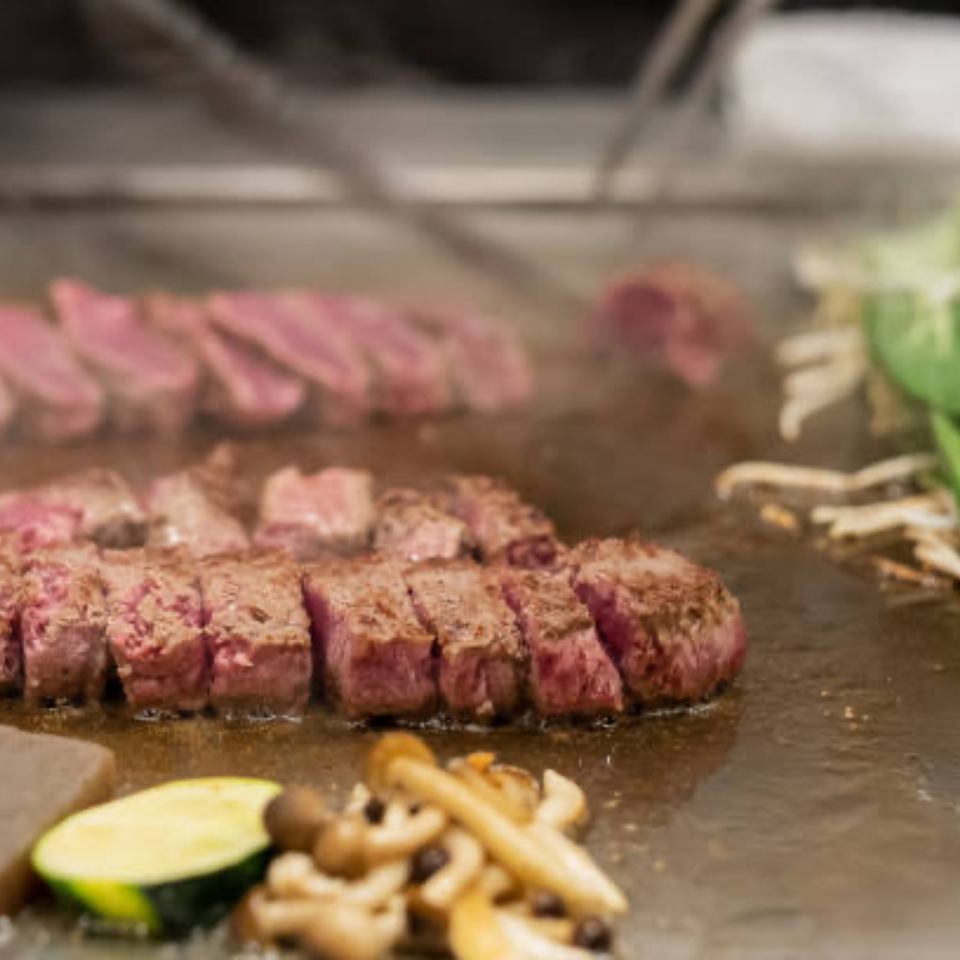 Sizzling steak and vegetables cooking on a teppanyaki grill at Tropical Sushi.