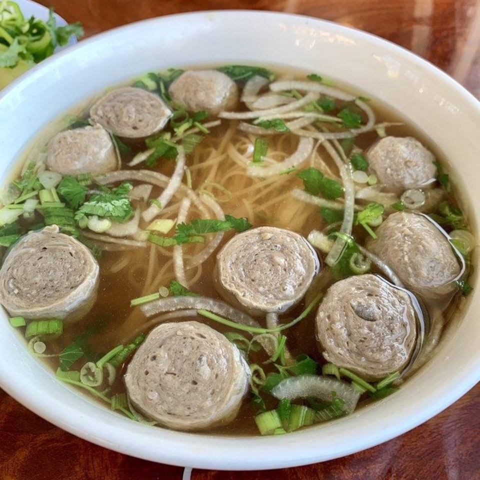 A bowl of Vietnamese pho with meatballs, noodles, onions, and green herbs.
